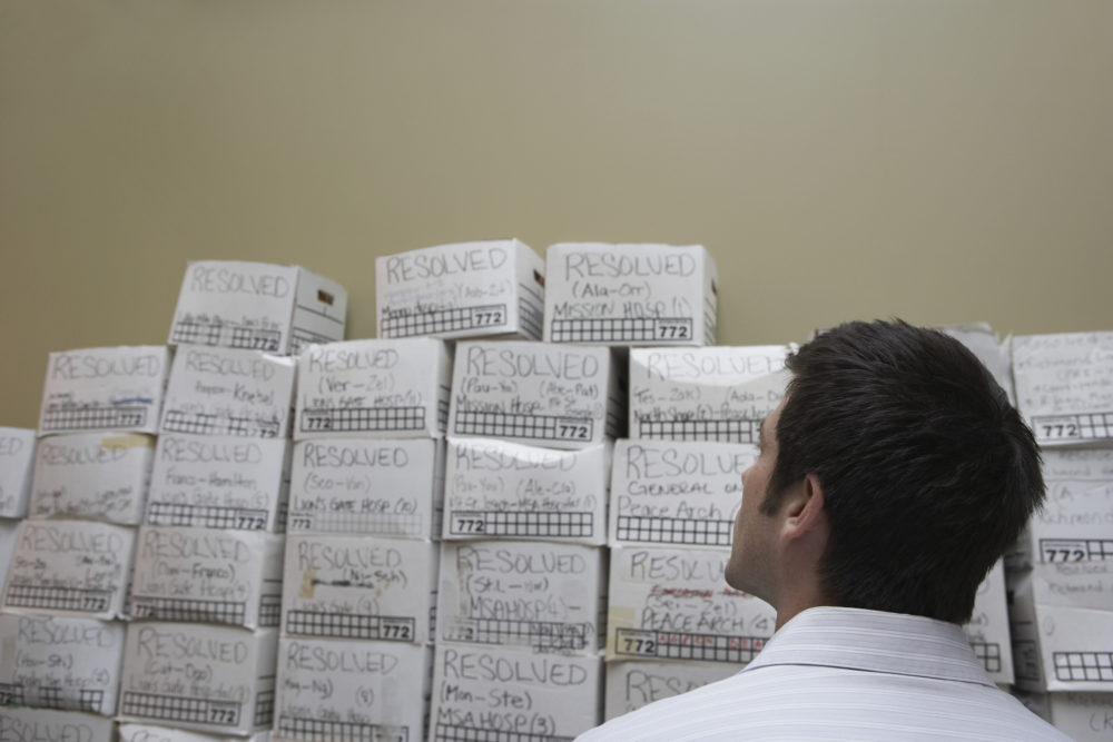 Business man standing in front of stack of filing boxes in storage room, back view, low angle view